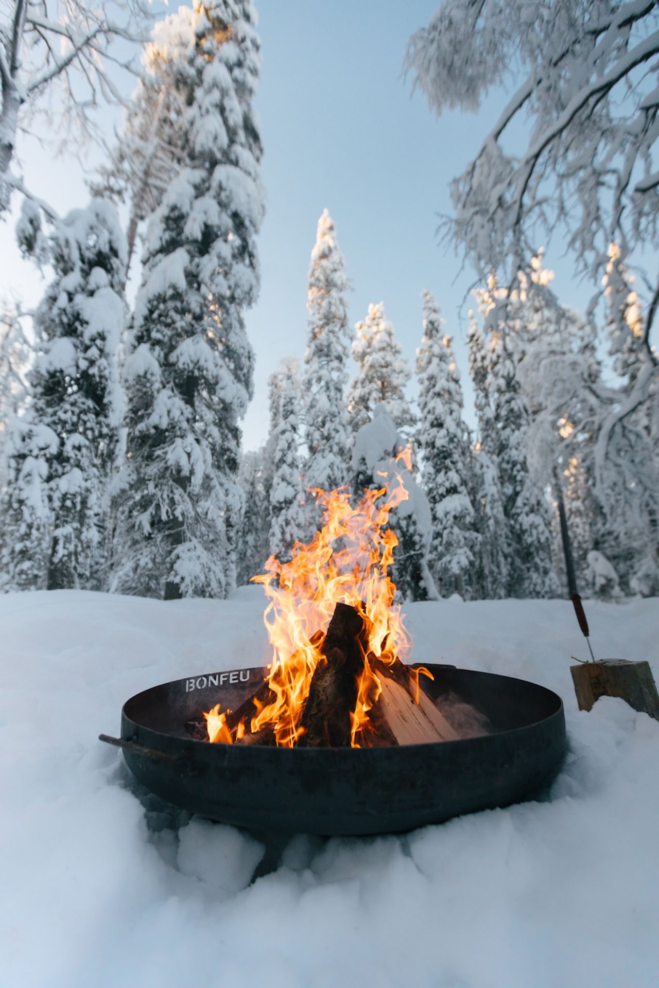 The open fire burning in the deep snow, ringed by tall snow-laden pines.
