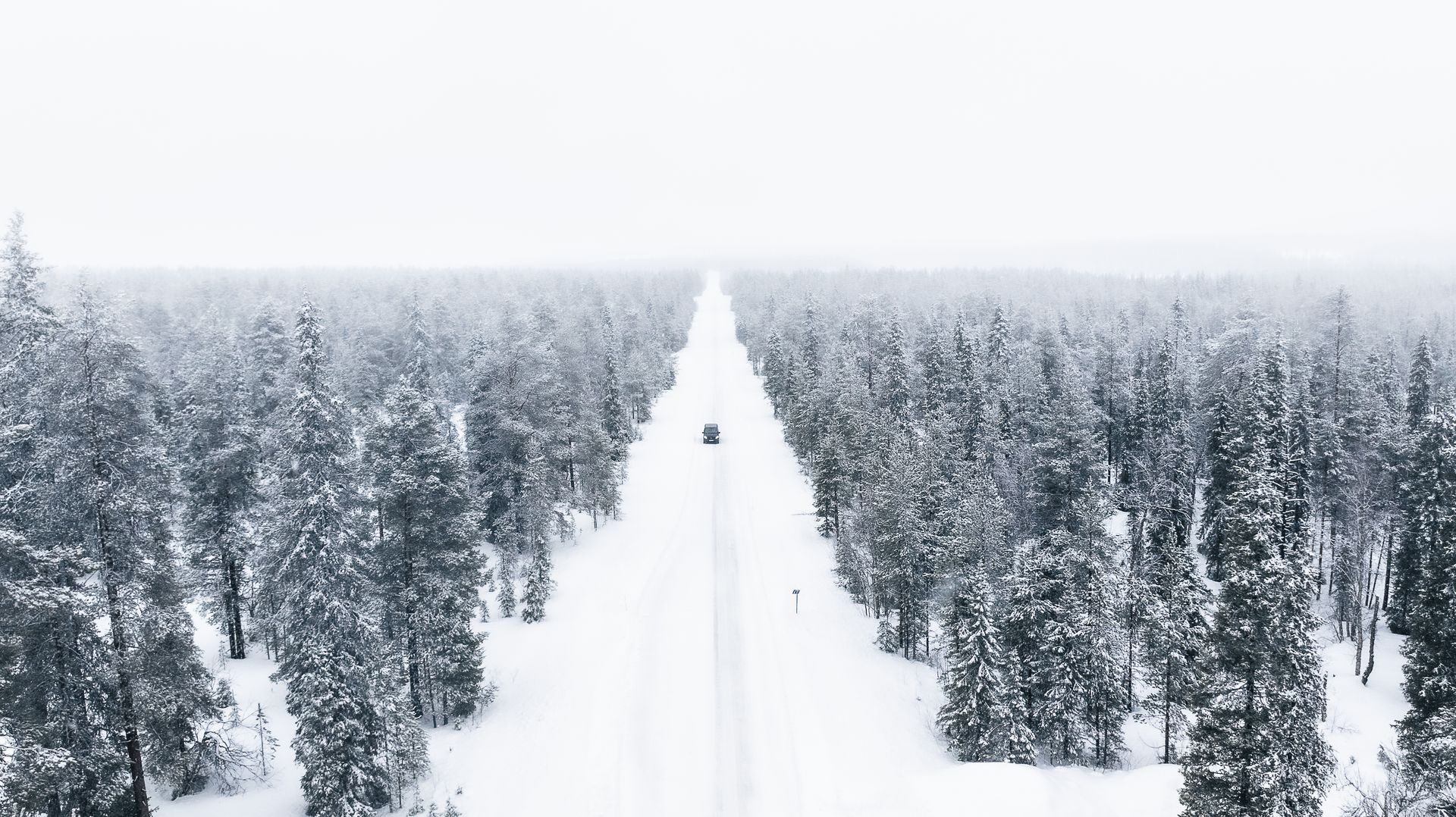 A single car on a snow-covered road through the Lapland forest.