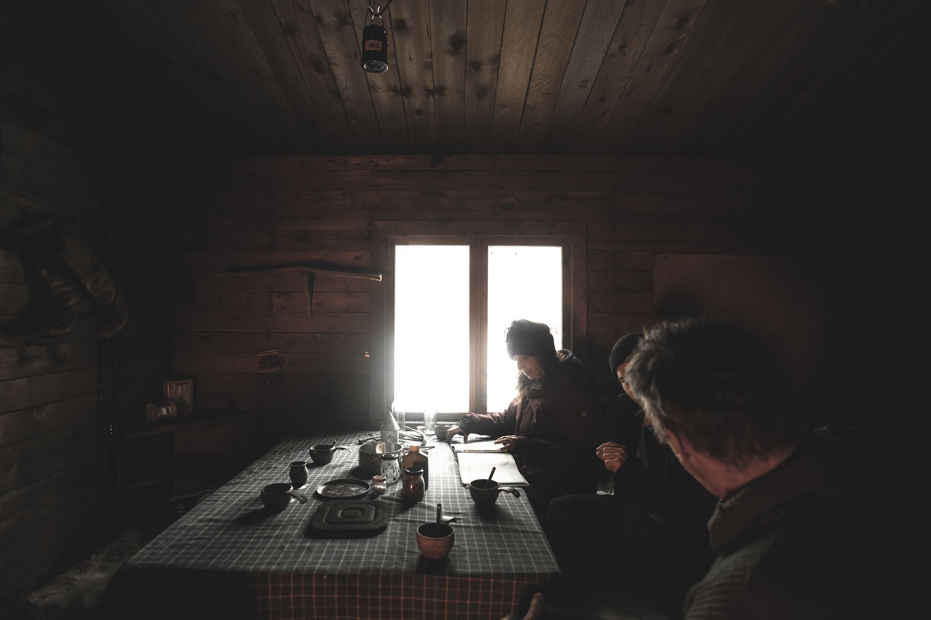 A long table set inside the herder's cabin, light pouring through a small window onto cups, bowls, and waiting hands.