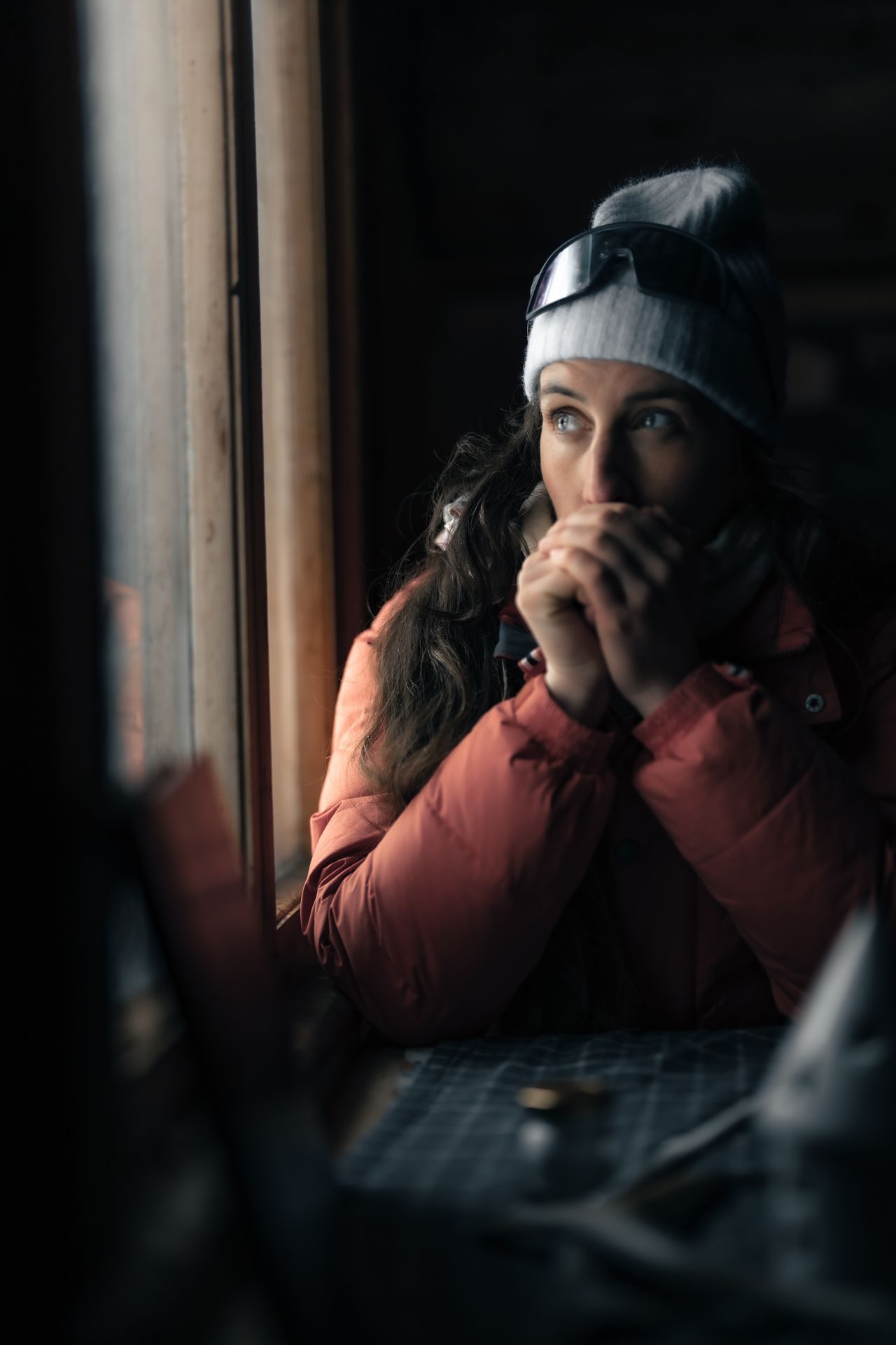 A guest at the cabin window, hands cupped against the cold, looking out into the arctic light.