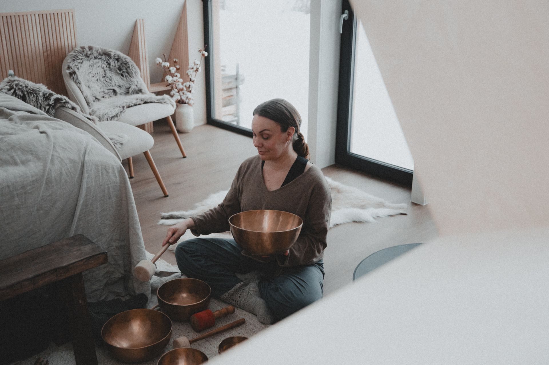 The practitioner seated on a sheepskin in the cabin, lifting a Tibetan singing bowl with mallet in hand, smaller bowls arranged in front.