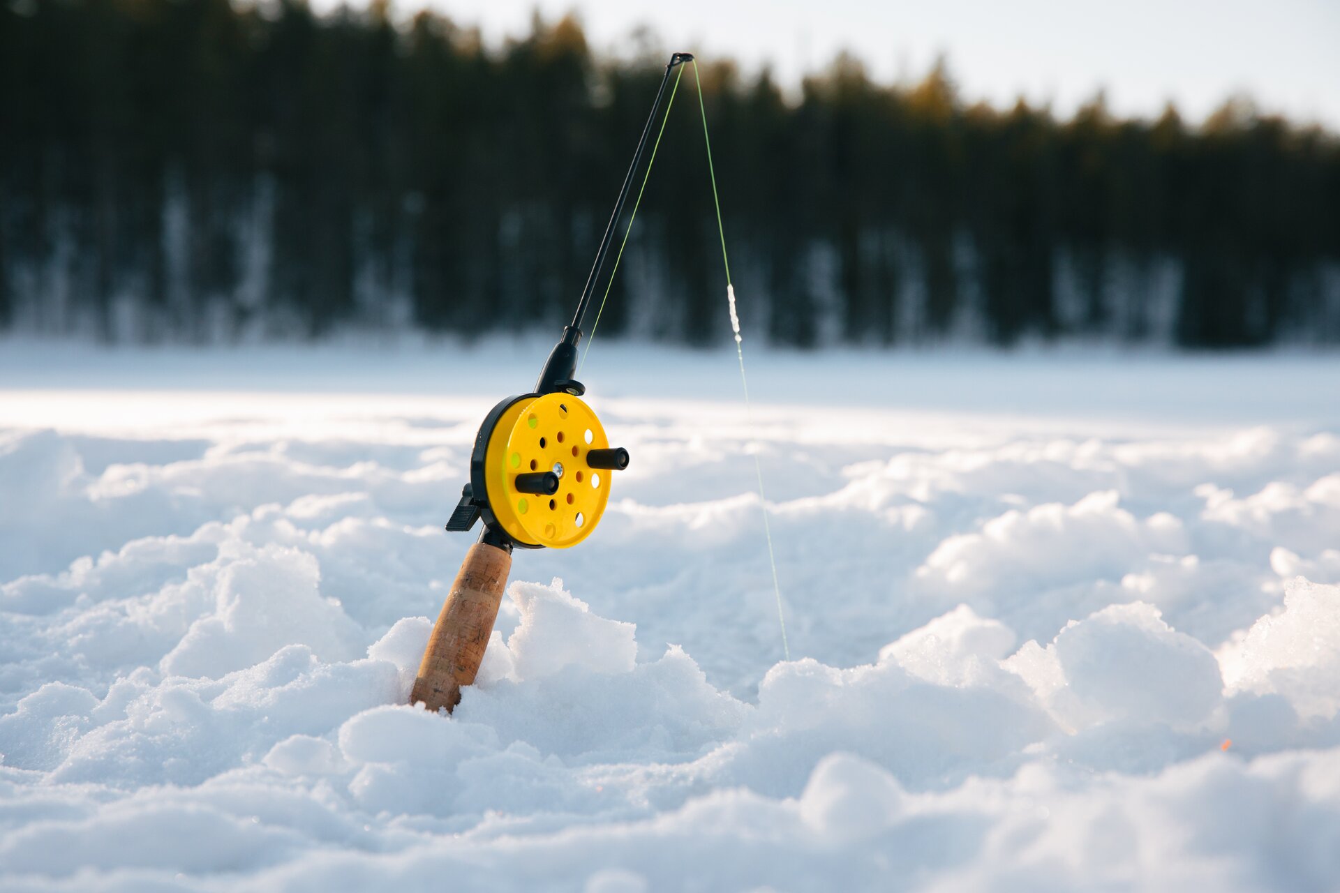 A figure crouched beside an auger-drilled hole in the ice of a frozen lake in Lapland.