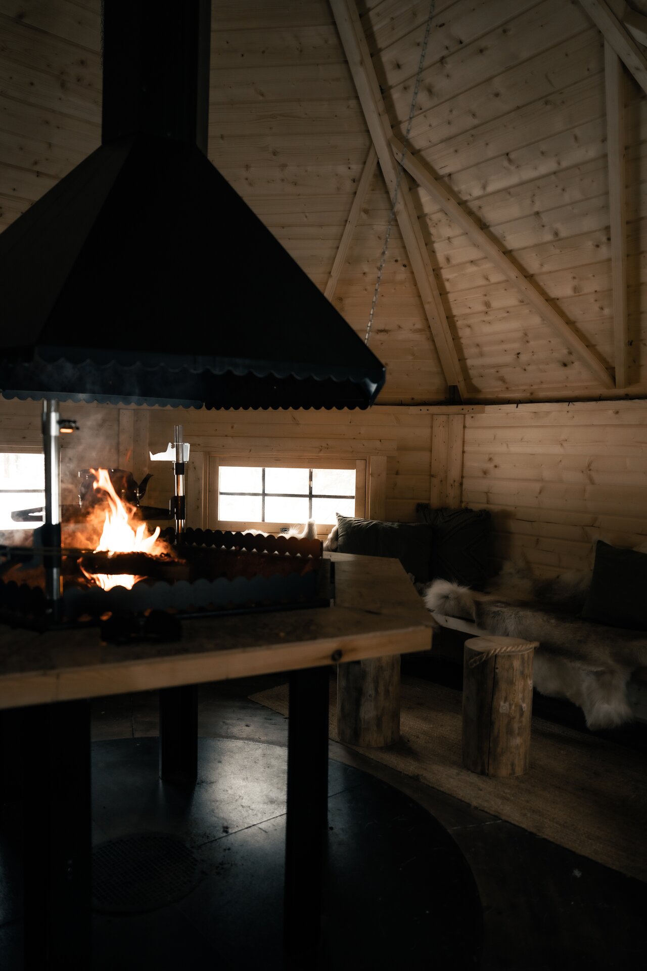 A glowing wooden kota at dusk, snow piled deep on its roof.