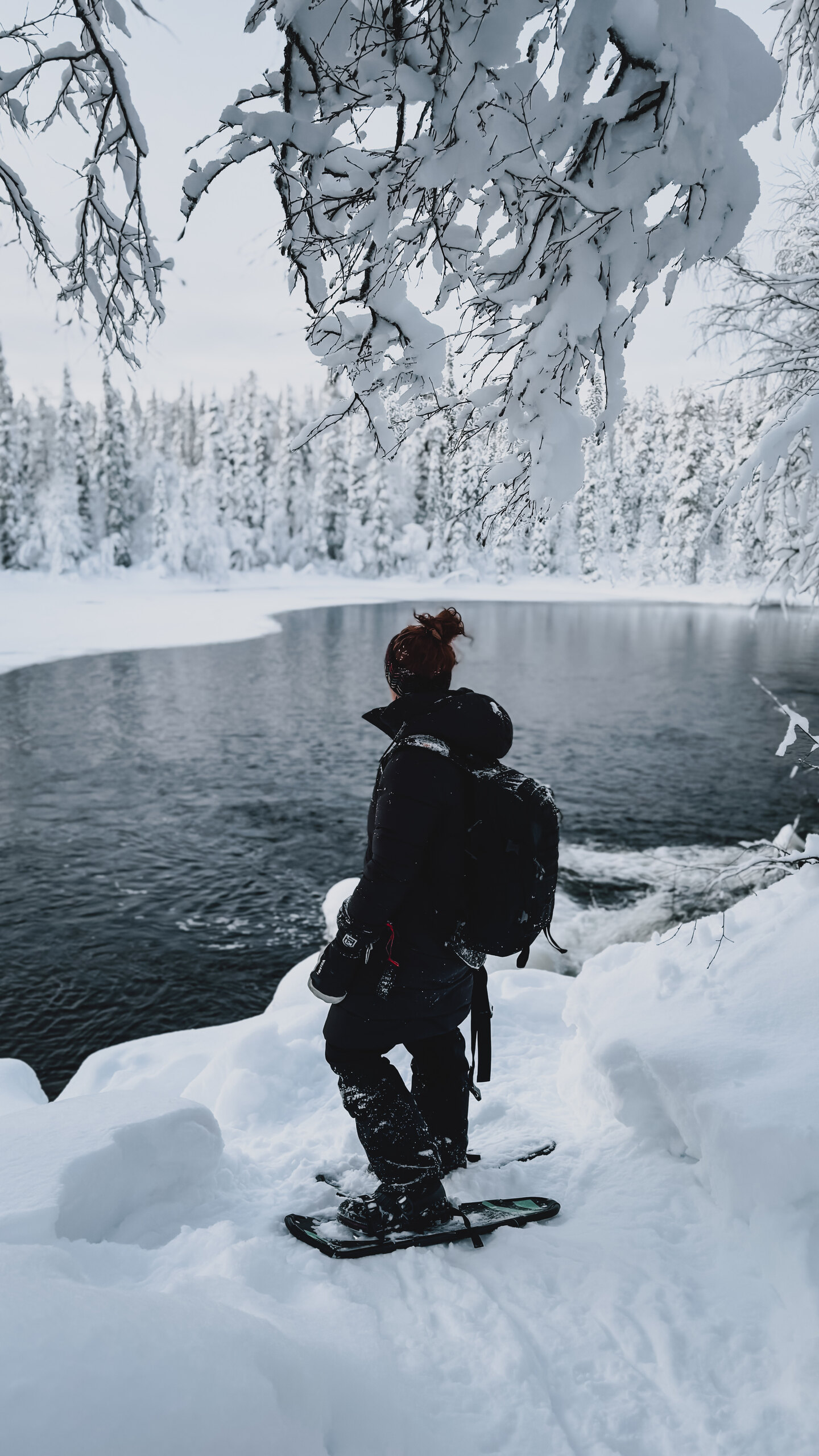 A snowshoe trail through deep arctic forest leading toward a restored 19th-century watermill.