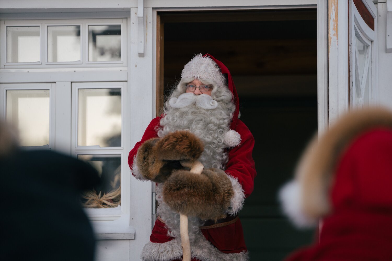 Santa with children at the cabin door, snow falling outside.