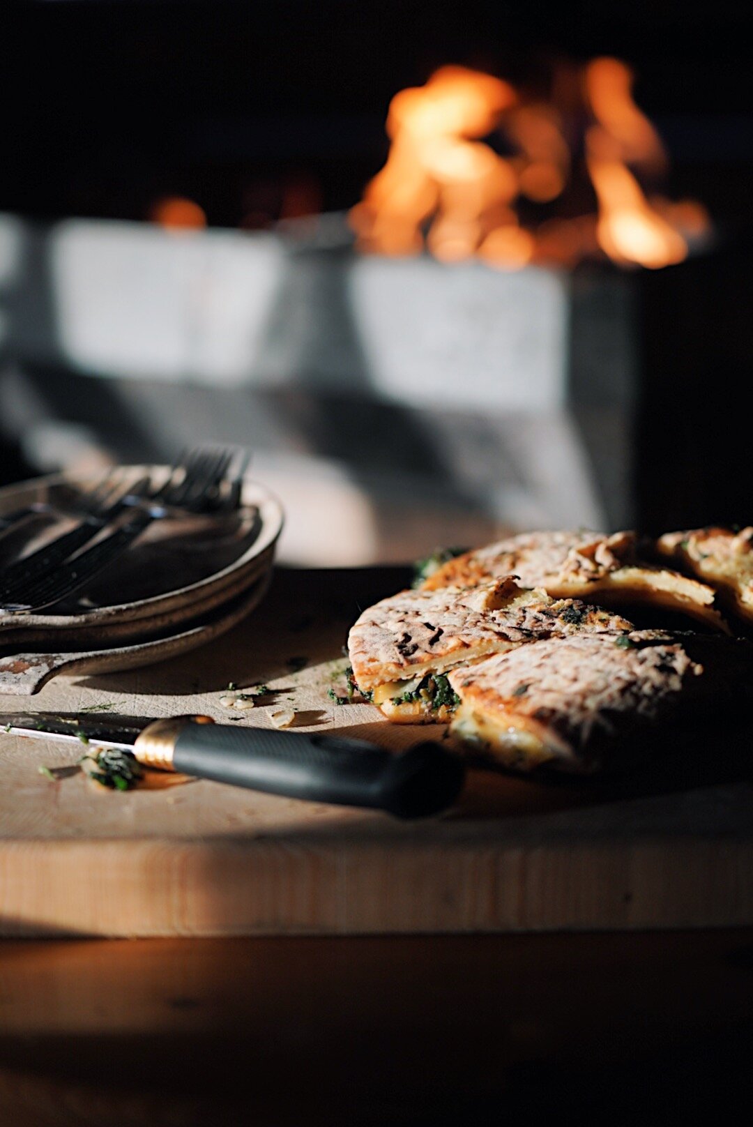 A homemade savoury pie sliced on a wooden board, fire glowing softly in the background.